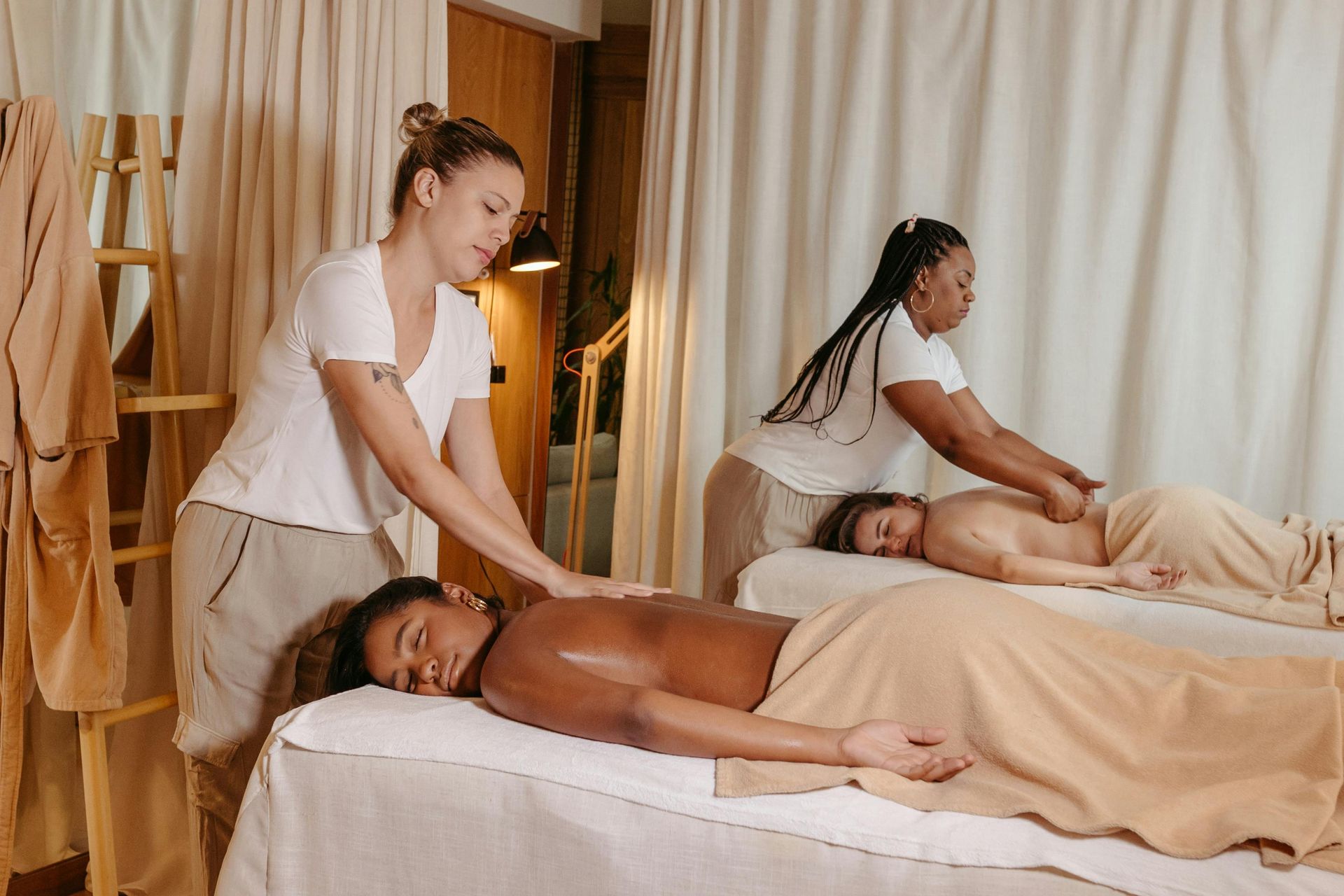 Two people receiving massages at a spa; two massage therapists work on their backs.