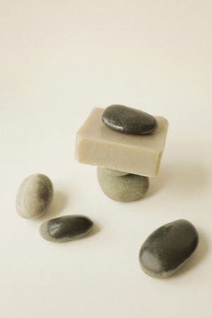 Stones and square soap arranged on a white surface. Gray, brown, and green tones create a spa-like setting.