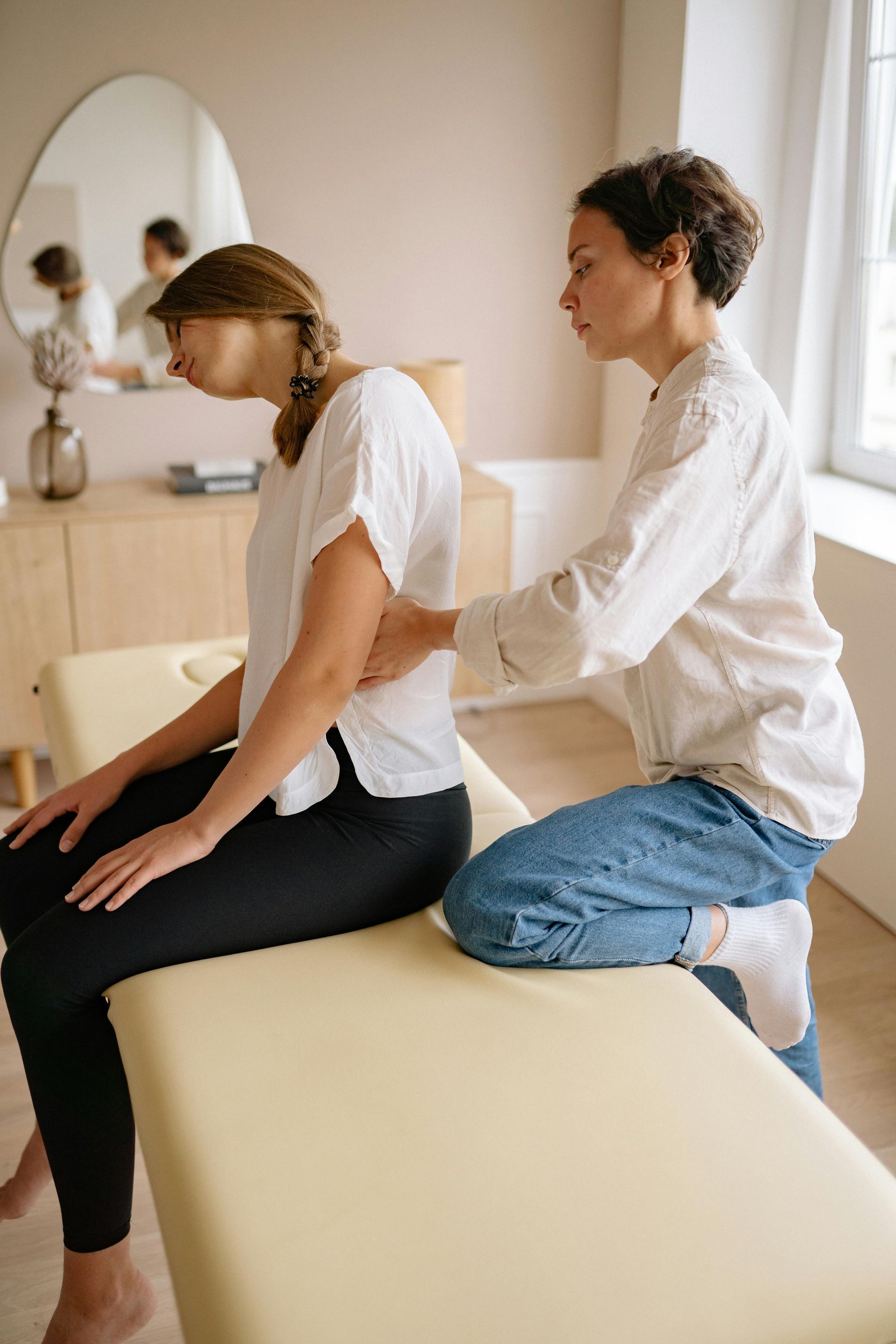 A woman receiving a back massage from another woman in a light-filled room.
