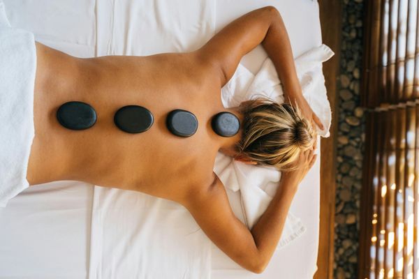Woman receiving hot stone massage on her back, lying on a white bed.