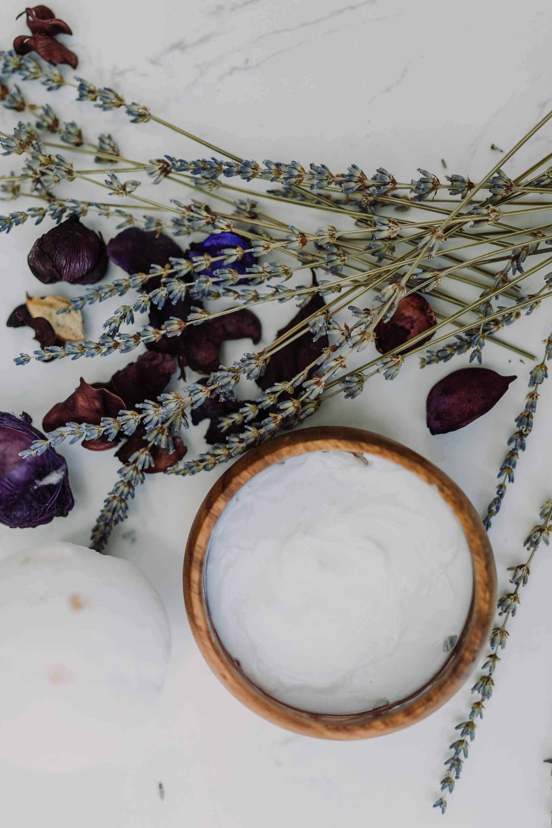 Wooden bowl of white powder, surrounded by lavender and dried flowers, on a white surface.