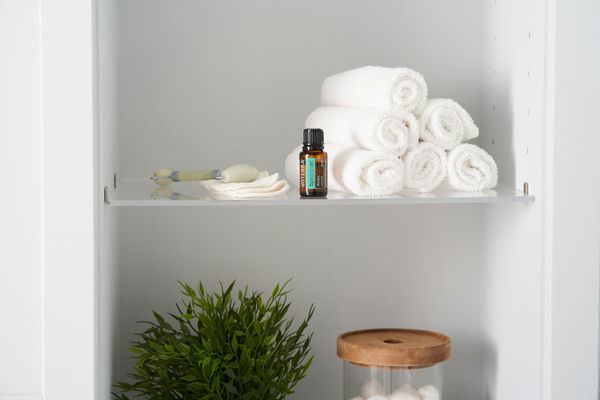 Bathroom shelf with rolled white towels, essential oil, jade roller, cotton pads, and plant.