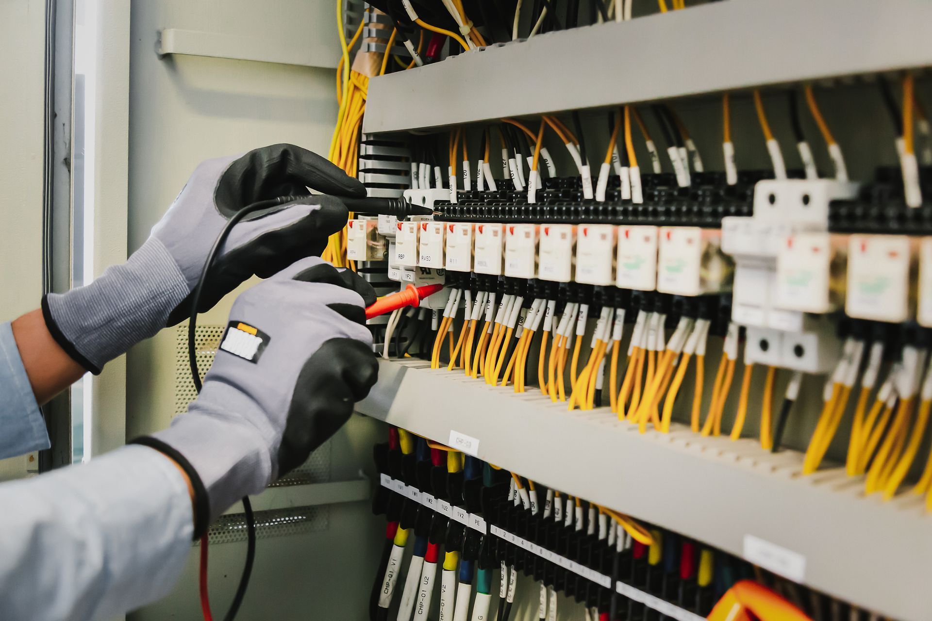 An electrician is working on an electrical panel with a multimeter.