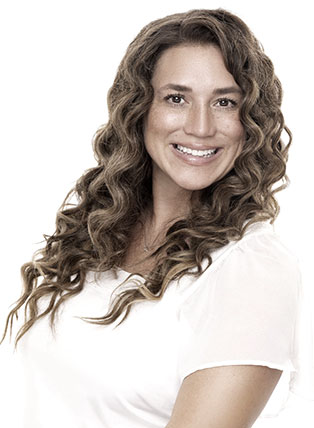 Woman with curly brown hair smiling, wearing a white top, looking at the camera.