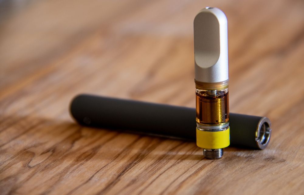 A close up of a vape pen and a cartridge on a wooden table.