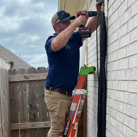 LCS Heating and Cooling - A man is standing on a ladder using a drill on a brick wall.