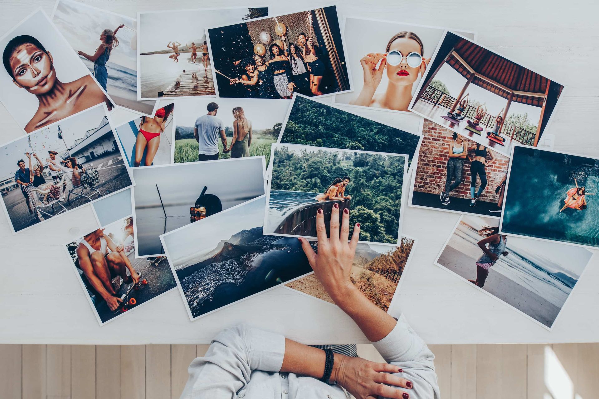 A person’s hand rests on a collection of various lifestyle photographs spread across a white surface.