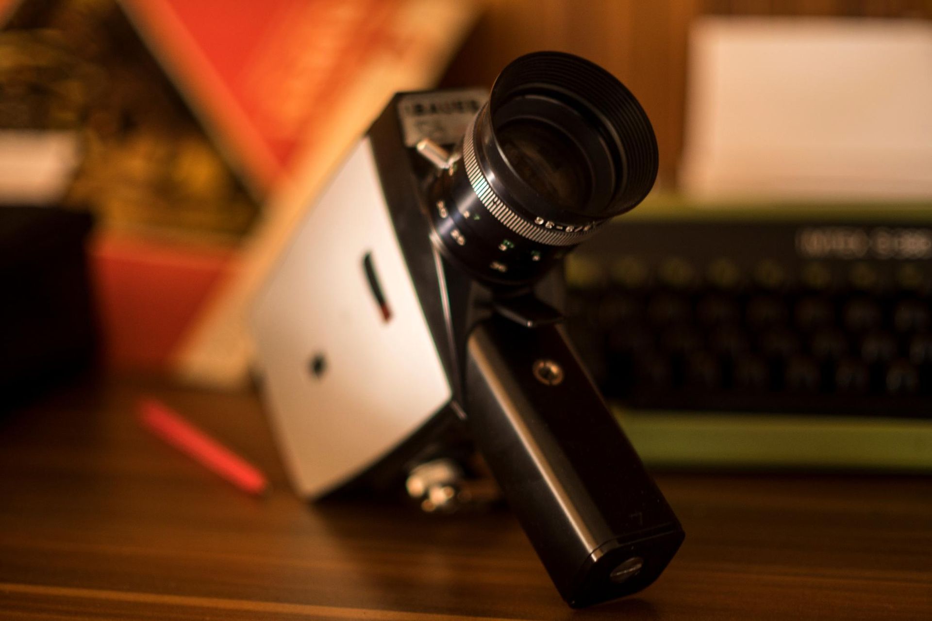 A vintage silver and black 8mm movie camera sits on a wooden desk next to a typewriter.