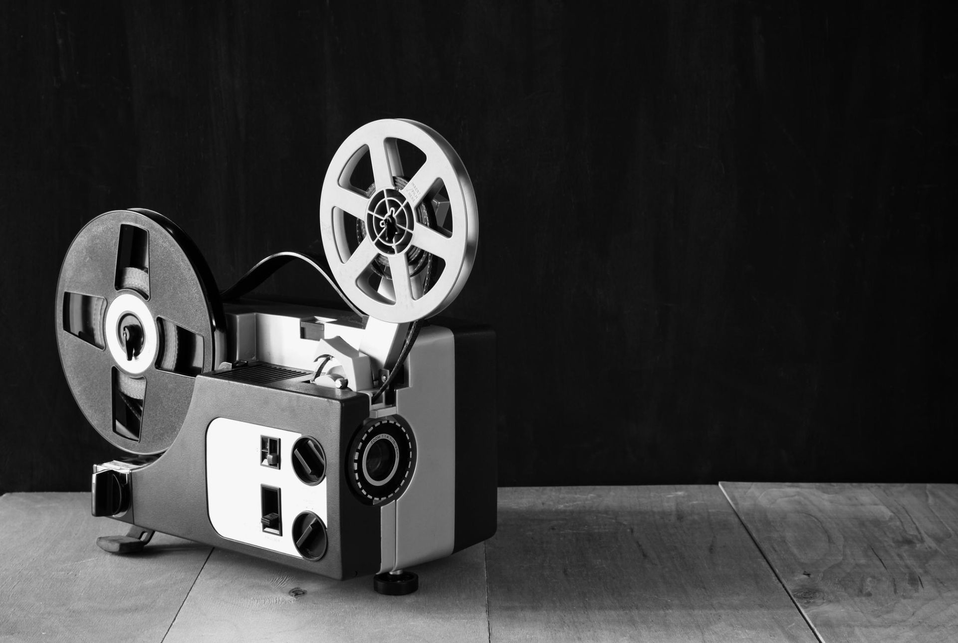 A black-and-white vintage film projector with two reels sitting on a wooden surface.