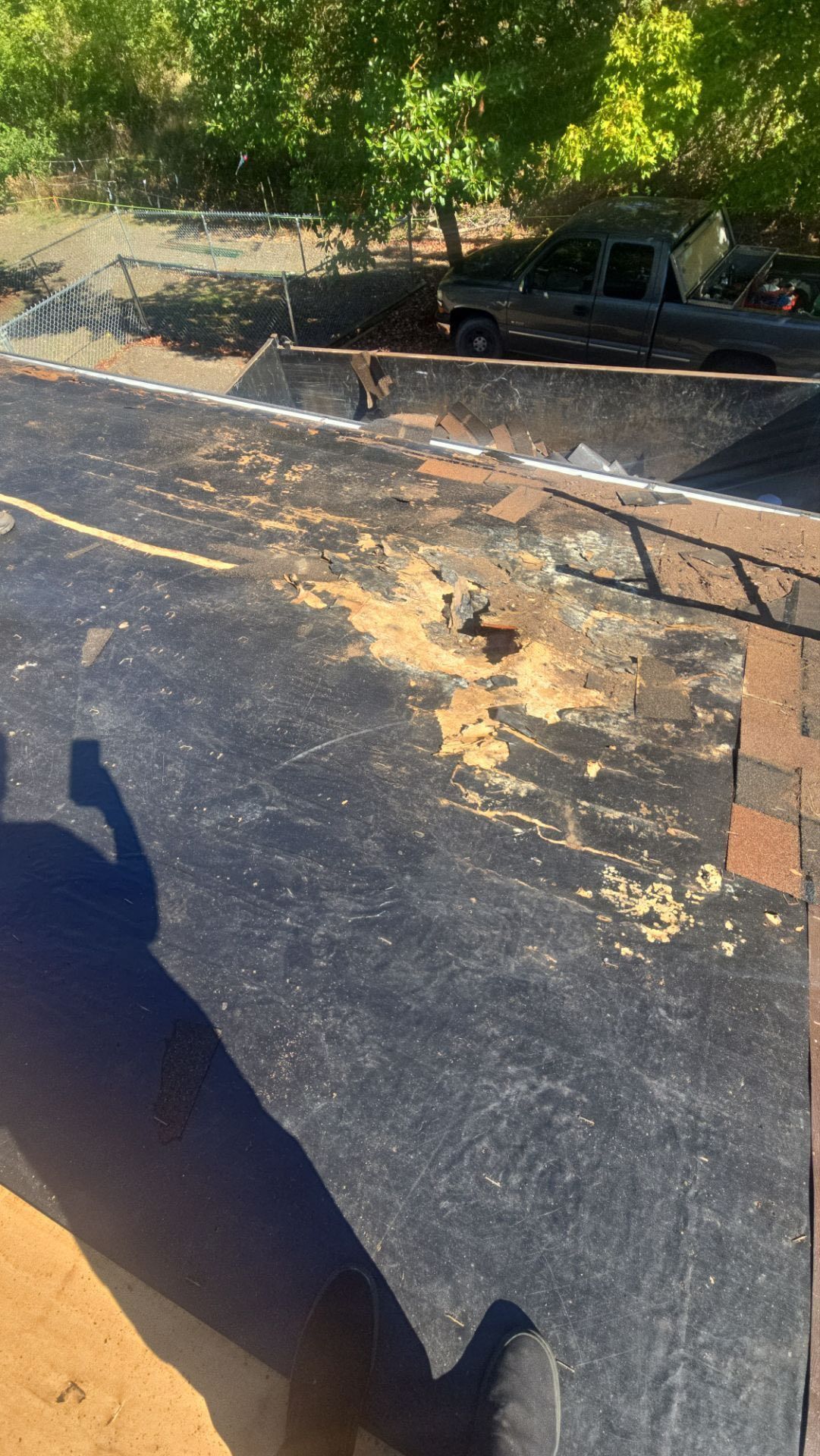 Roof with exposed underlayment; a truck and trees are visible in the background.