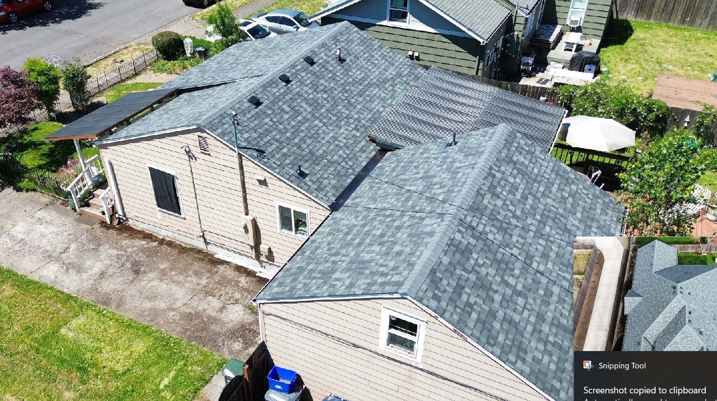 Overhead view of a house with a gray shingle roof and green lawn in a residential area.