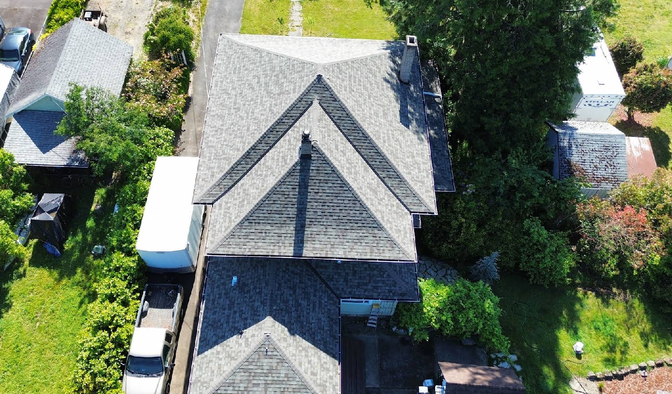 Overhead view of a house with a gray roof, surrounded by green trees and grass, on a sunny day.