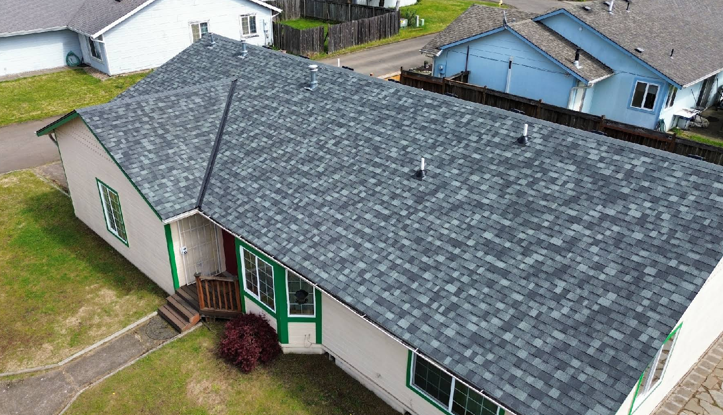 Aerial view of a house with a gray shingle roof, green trim, and a small front yard with a walkway.