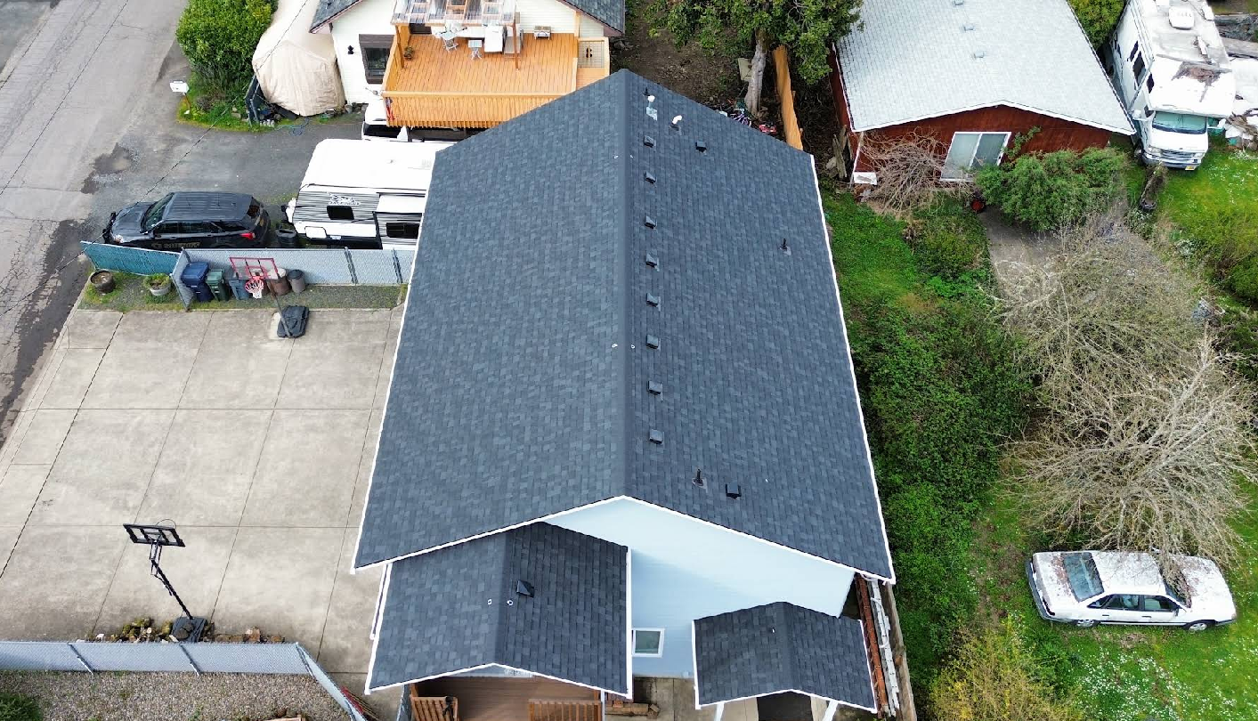 Aerial view of a blue house with dark gray roof surrounded by neighboring homes and vehicles.