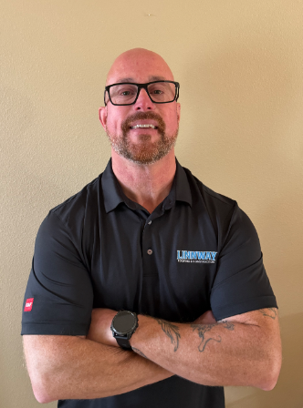 Man in sunglasses and gray polo shirt in a vehicle, smiling.