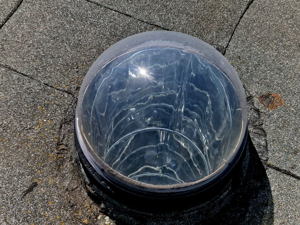 Clear, domed skylight on a dark asphalt shingle roof.