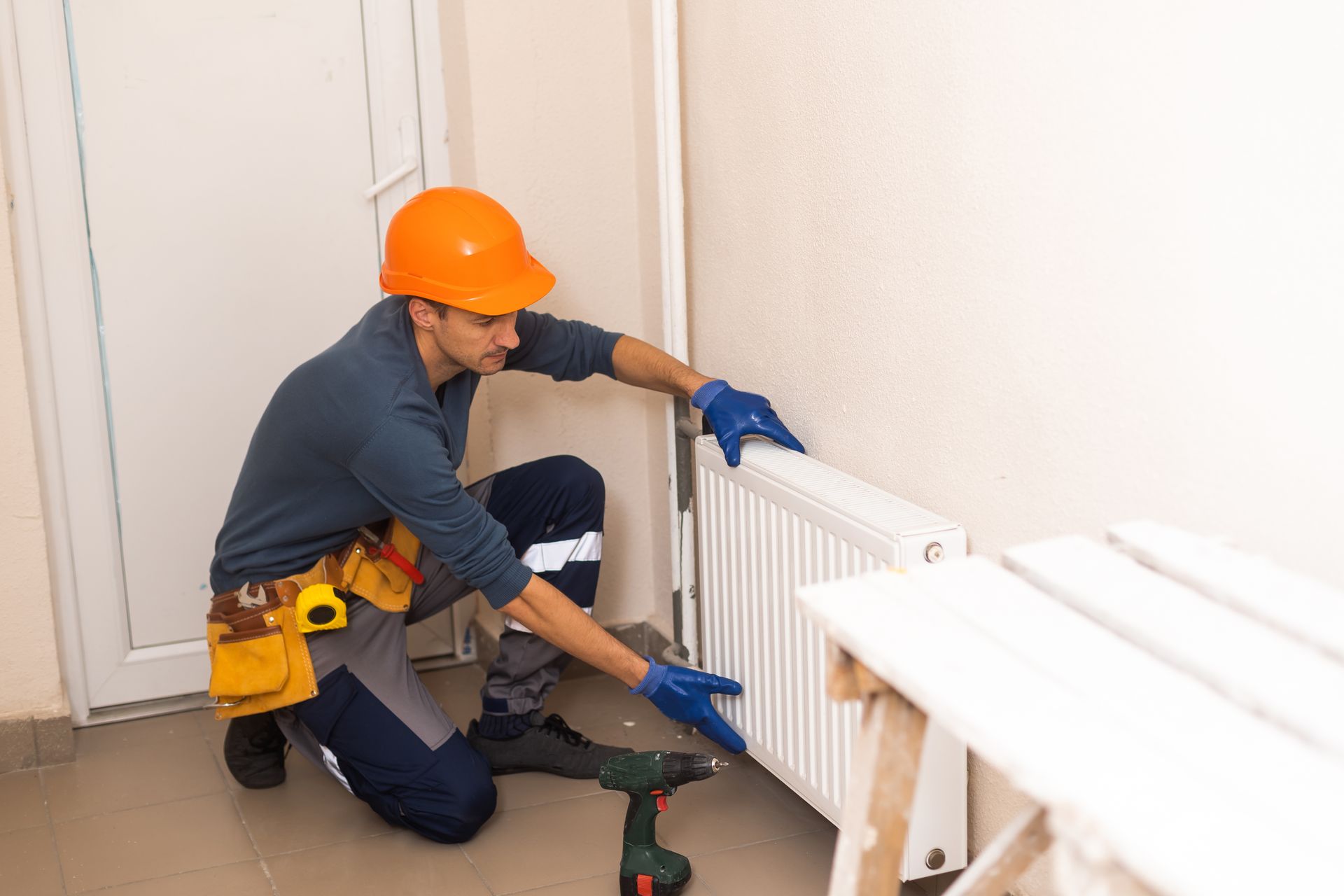Worker in orange hard hat installing a radiator with a wrench in a hallway