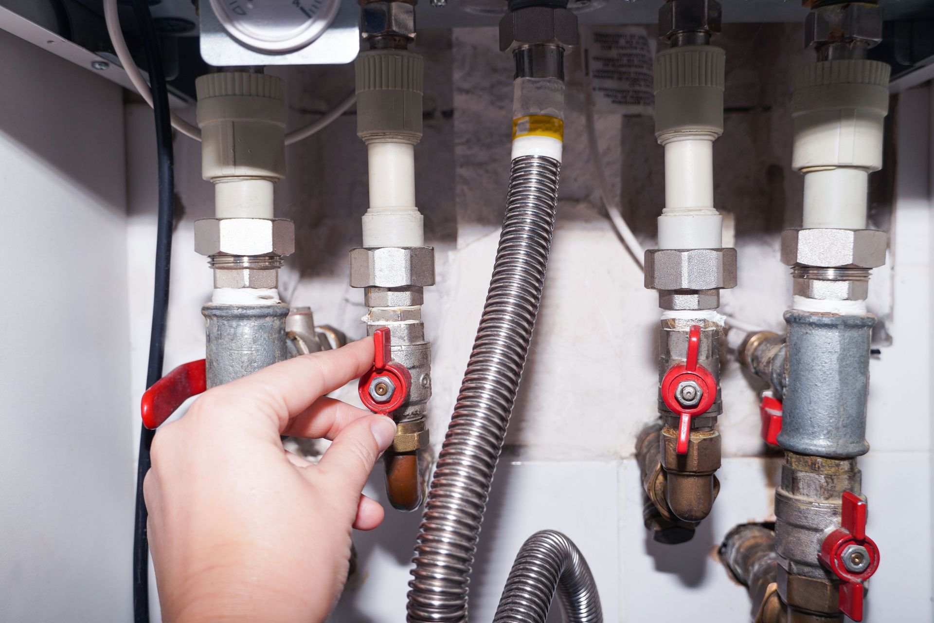 Hand turning a red valve on plumbing pipes under a sink