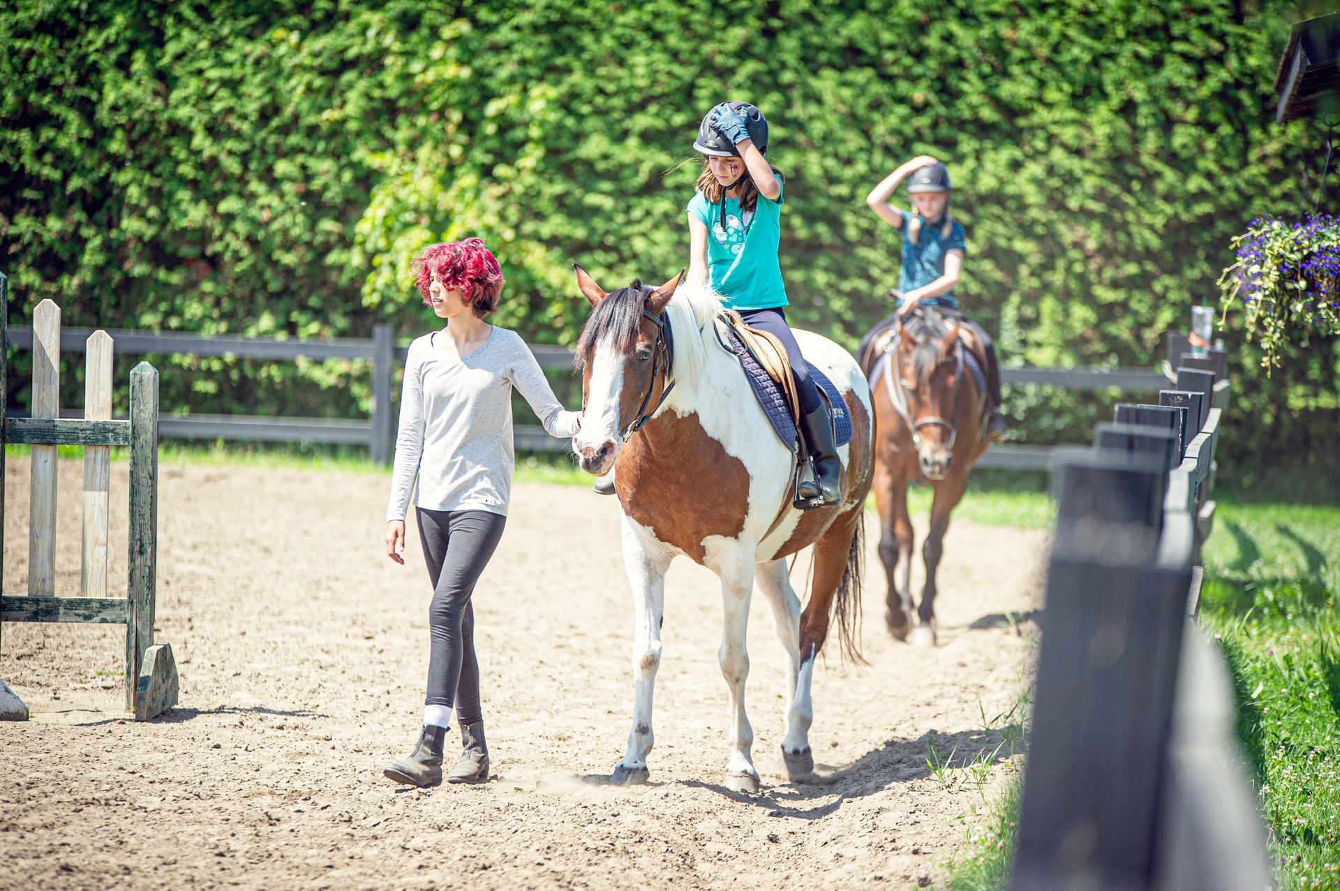 A woman is walking a child on a horse in a fenced in area.