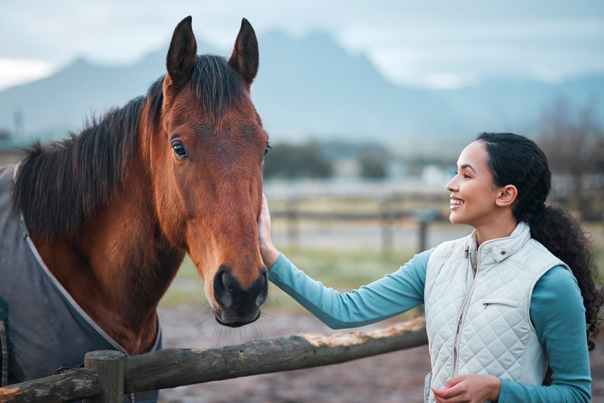 A woman is petting a brown horse behind a wooden fence.