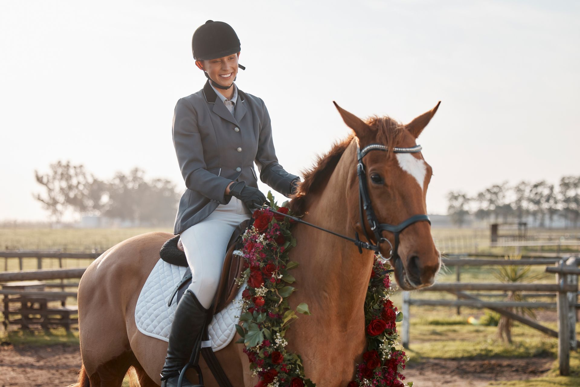 A woman is riding a brown horse with a wreath around its neck.