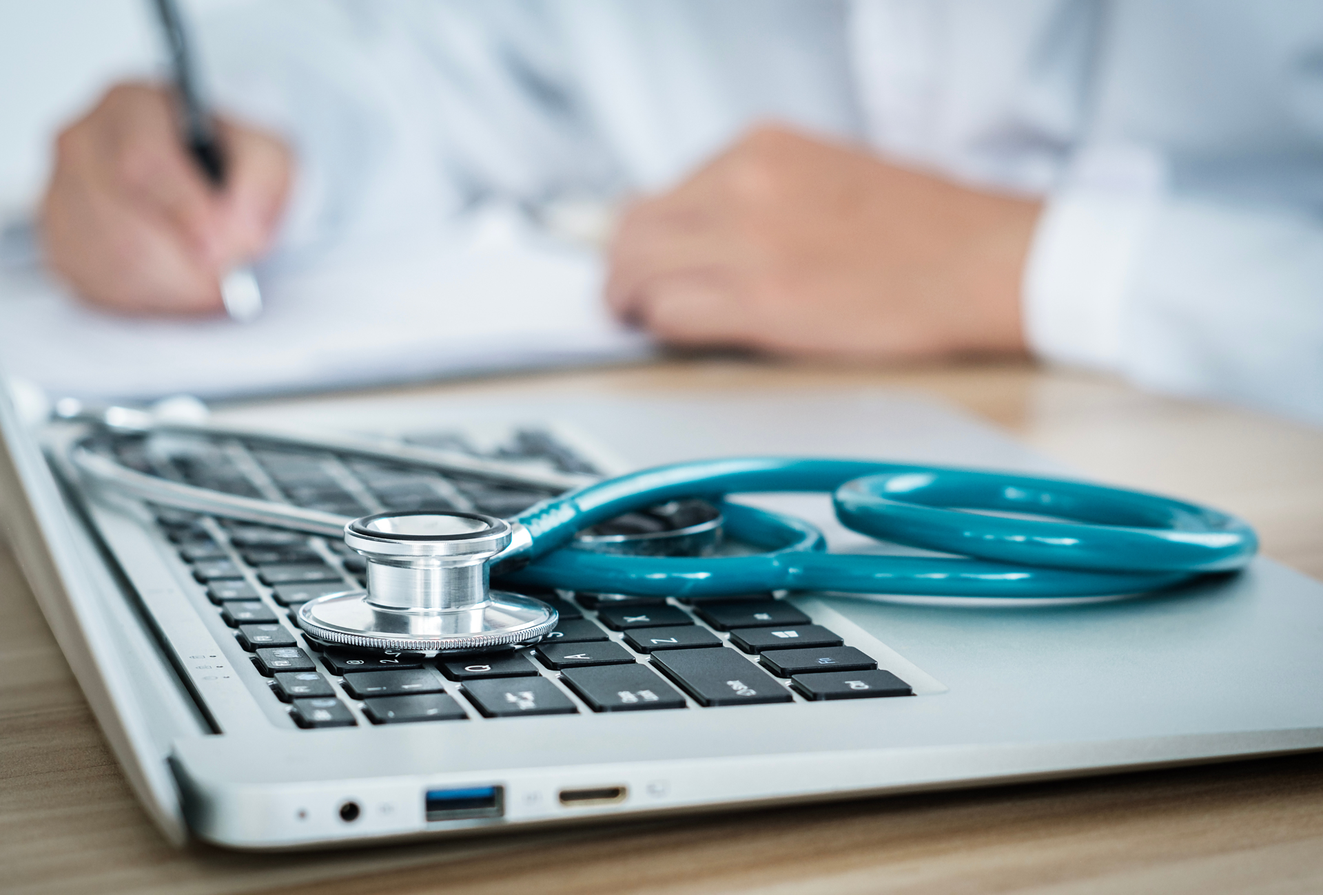 A doctor working next to a laptop and a stethoscope. 