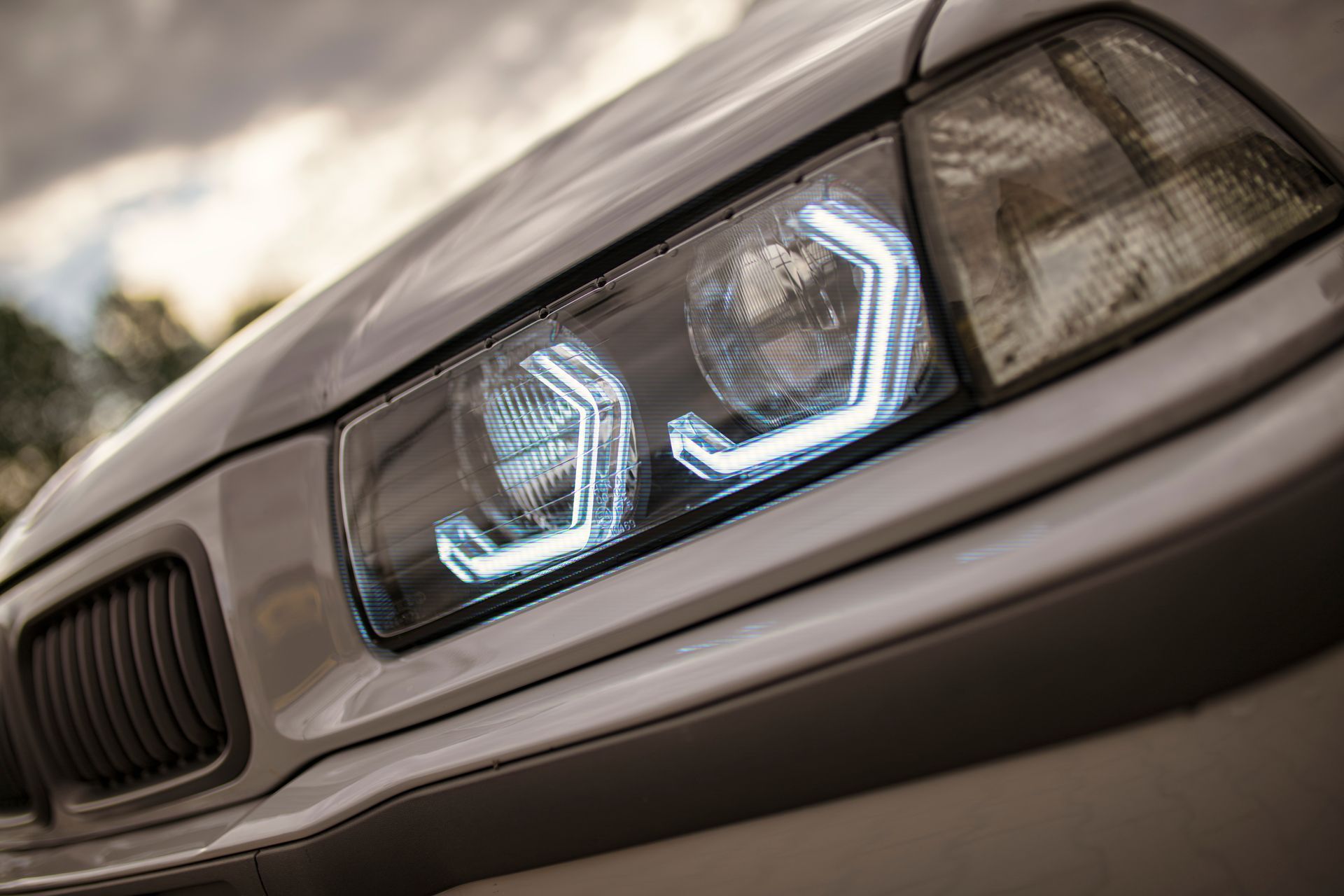 Close-up of a silver car's headlight with white, geometric LED accents and a black grille.