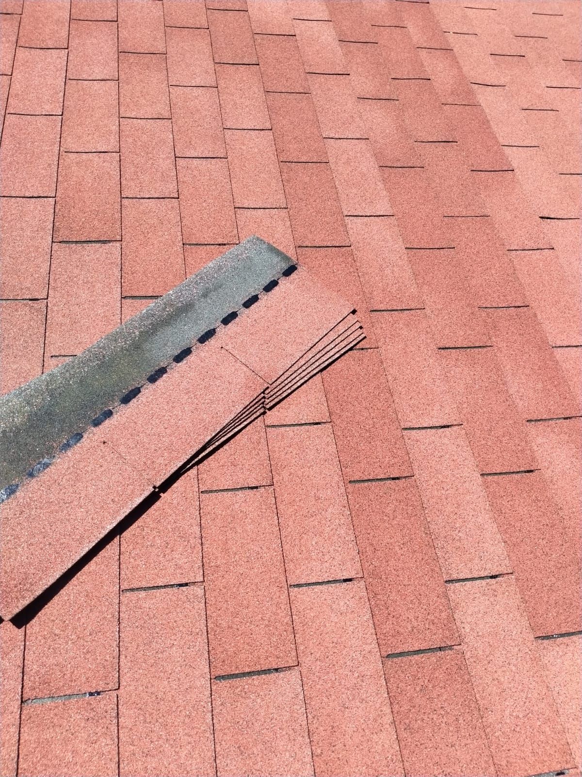 Tetto con tegole di asfalto rosse, con una pila di tegole nuove nelle vicinanze.