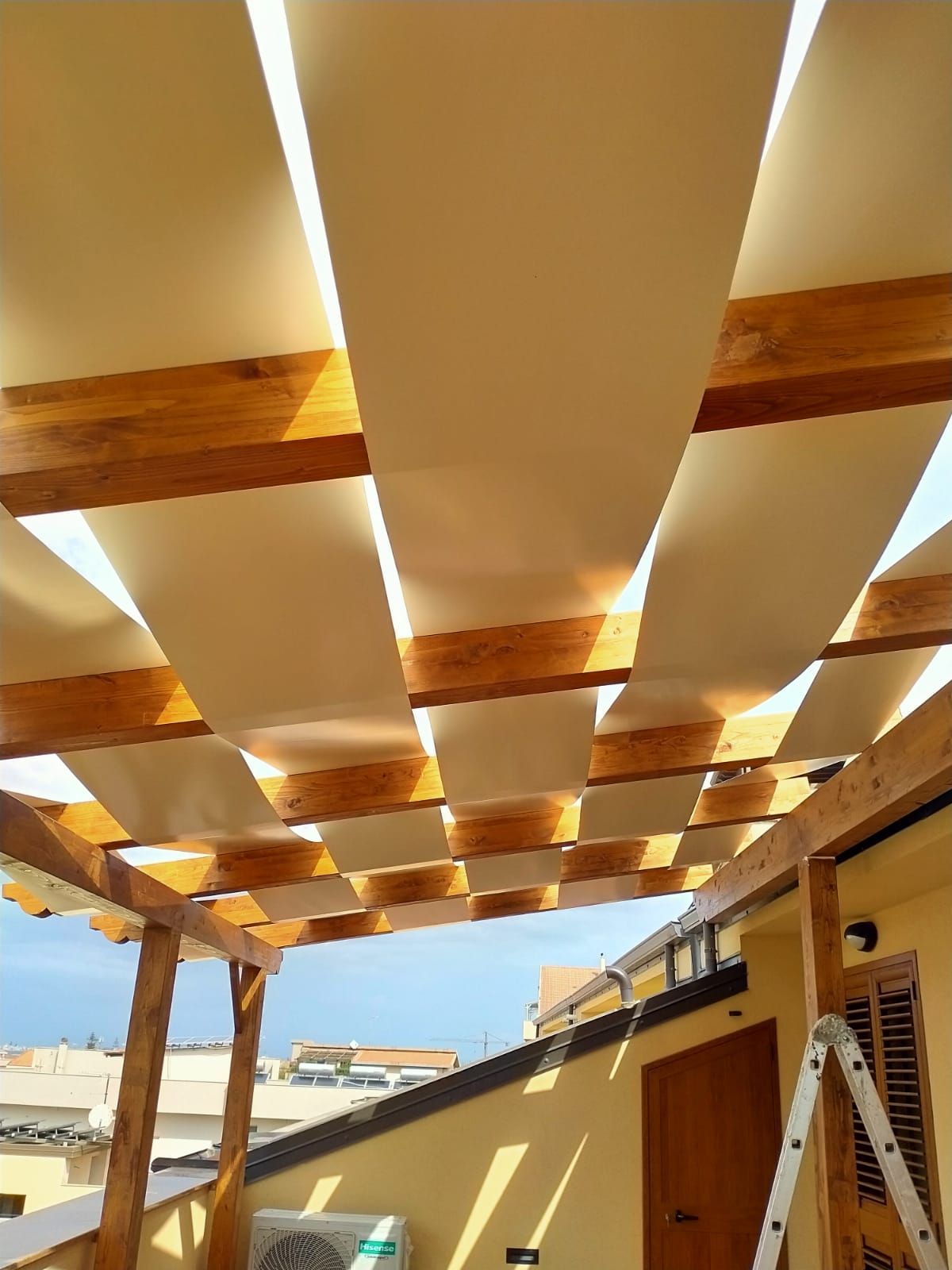 Pergola in legno con tenda in tessuto color cuoio, su un tetto.