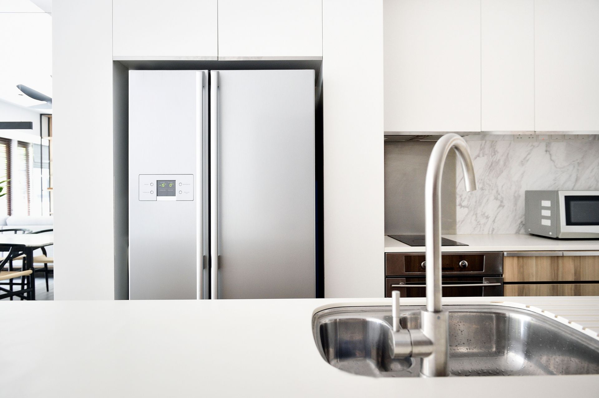Stainless steel refrigerator in white kitchen with sink.