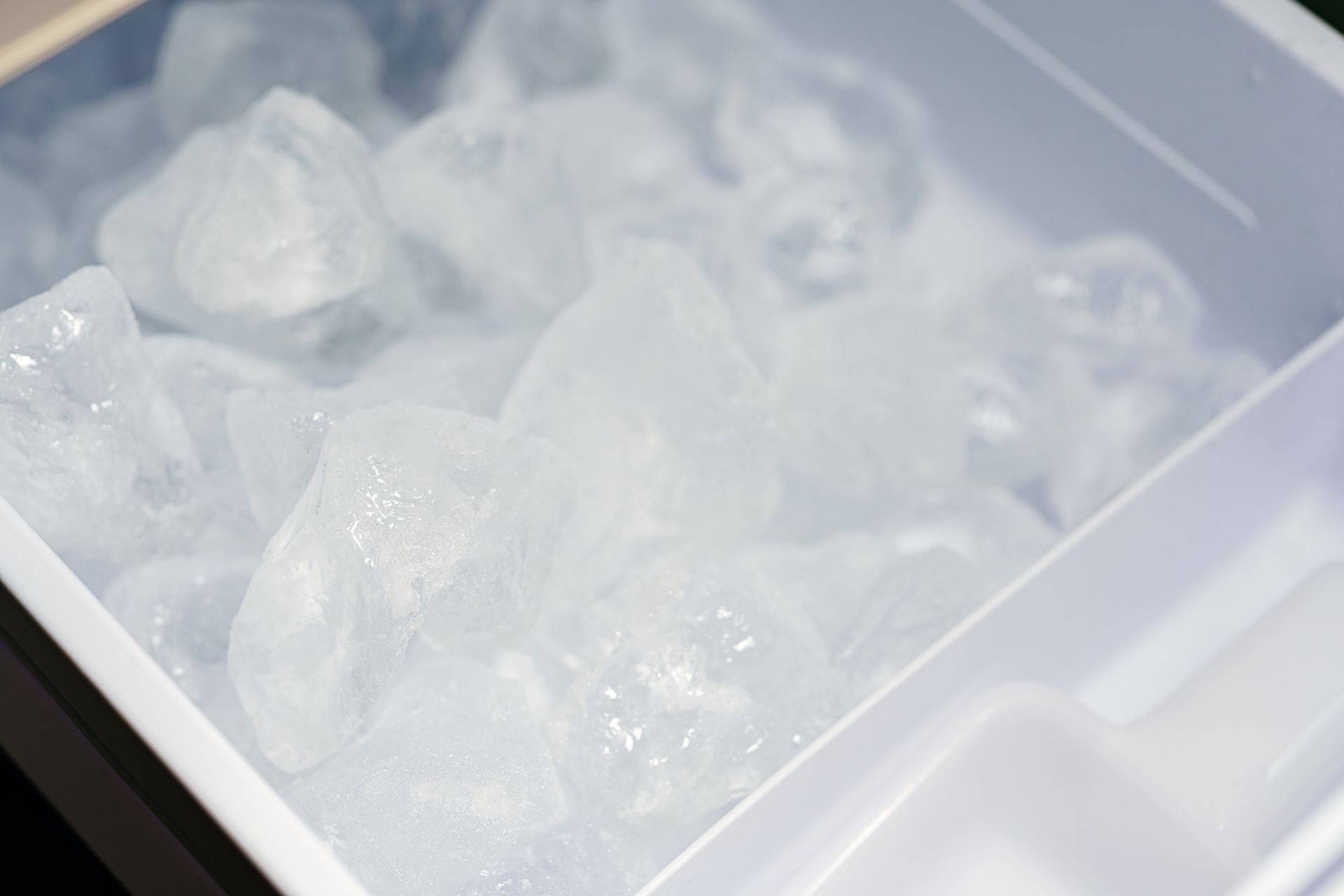 Ice cubes in a white ice maker tray, with a white scoop visible in the corner.