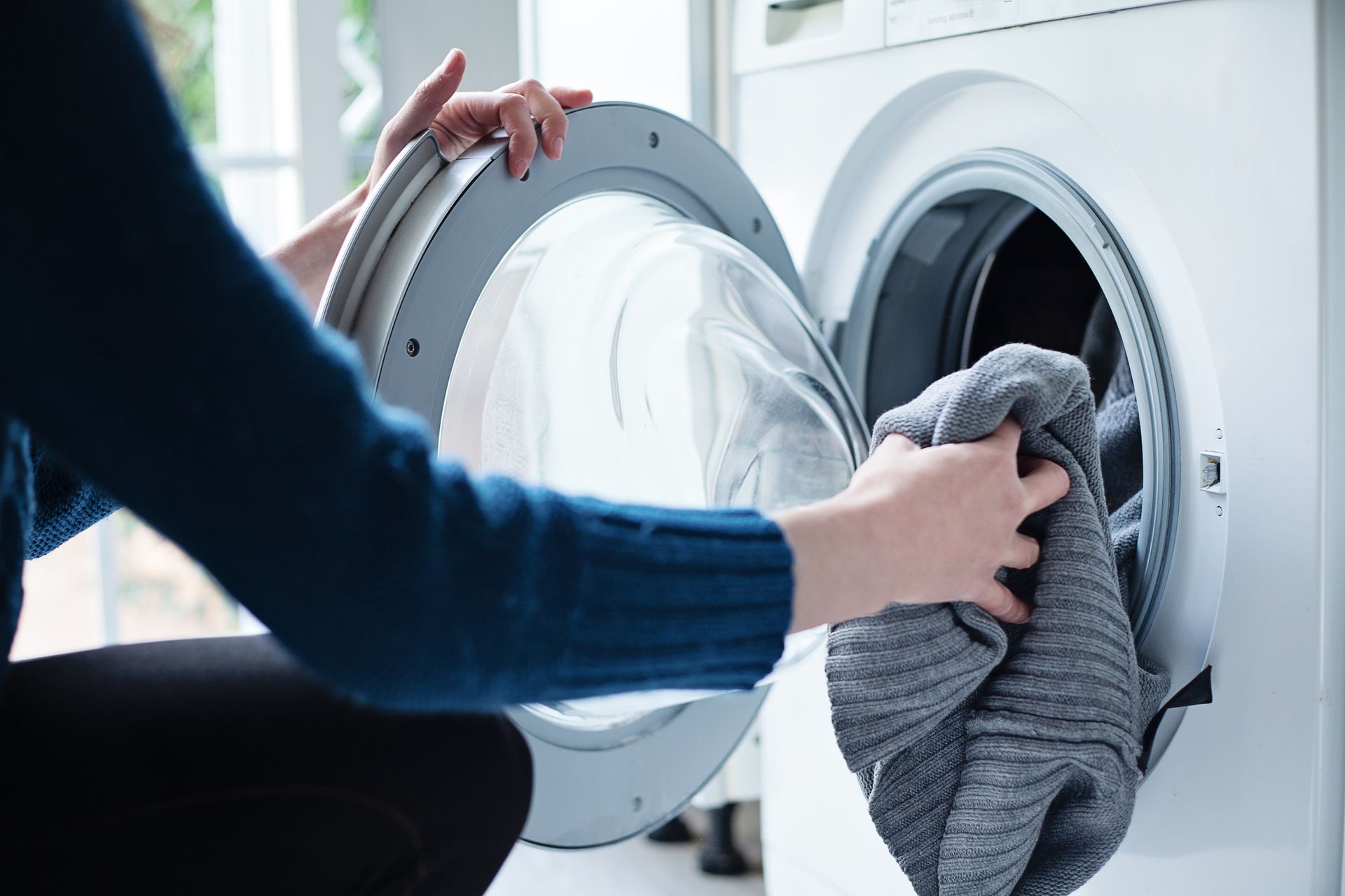 Person loading clothes into a washing machine.