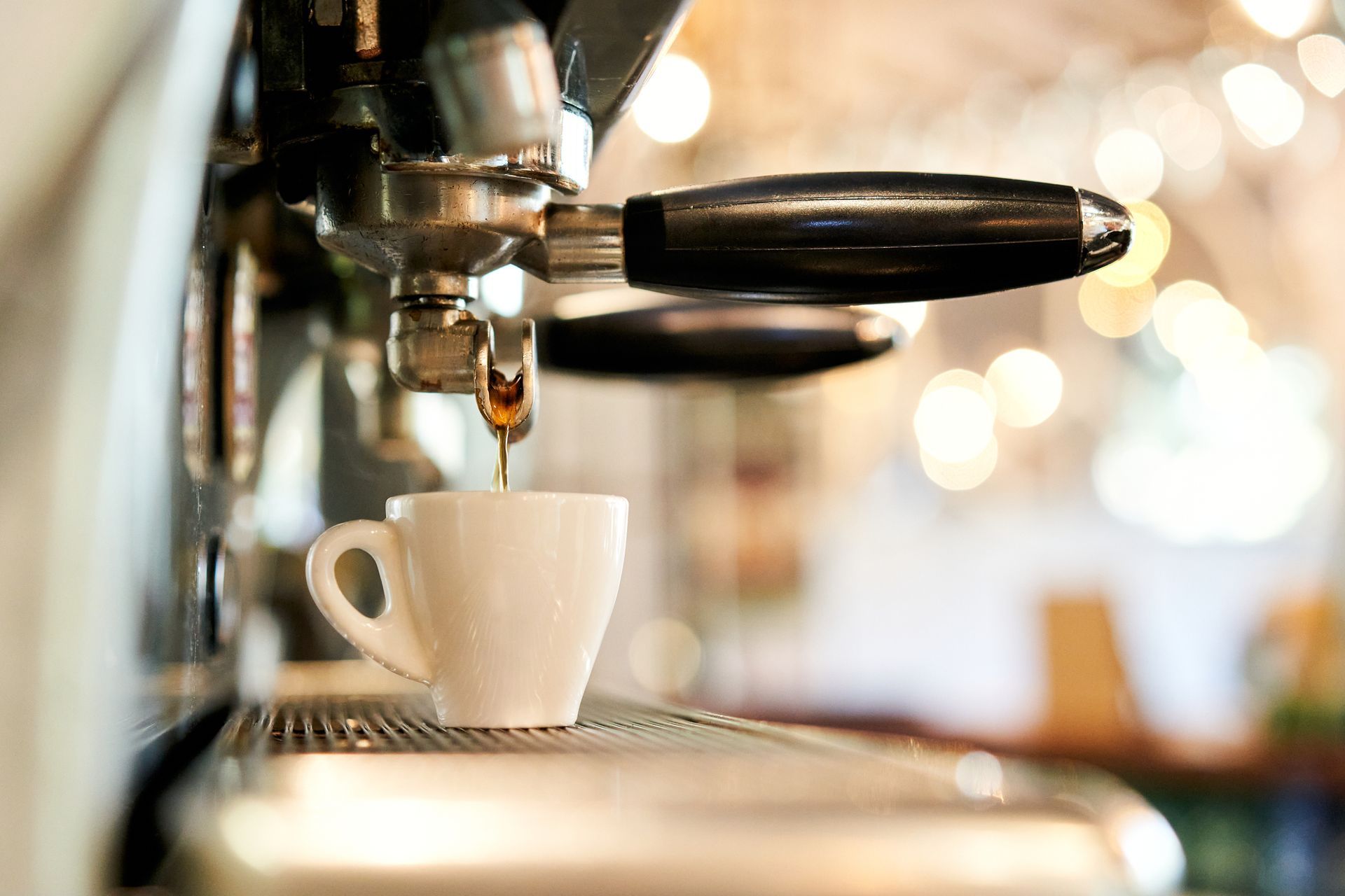 Espresso machine dispensing coffee into a white cup, blurred cafe background.