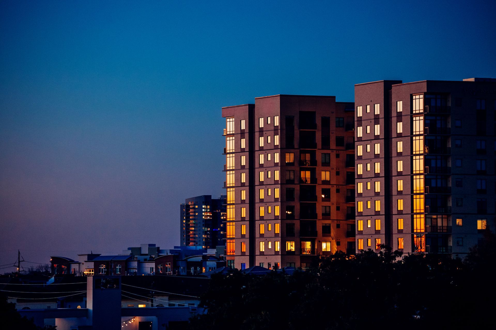 Skyscrapers with lit windows at dusk against a blue sky.