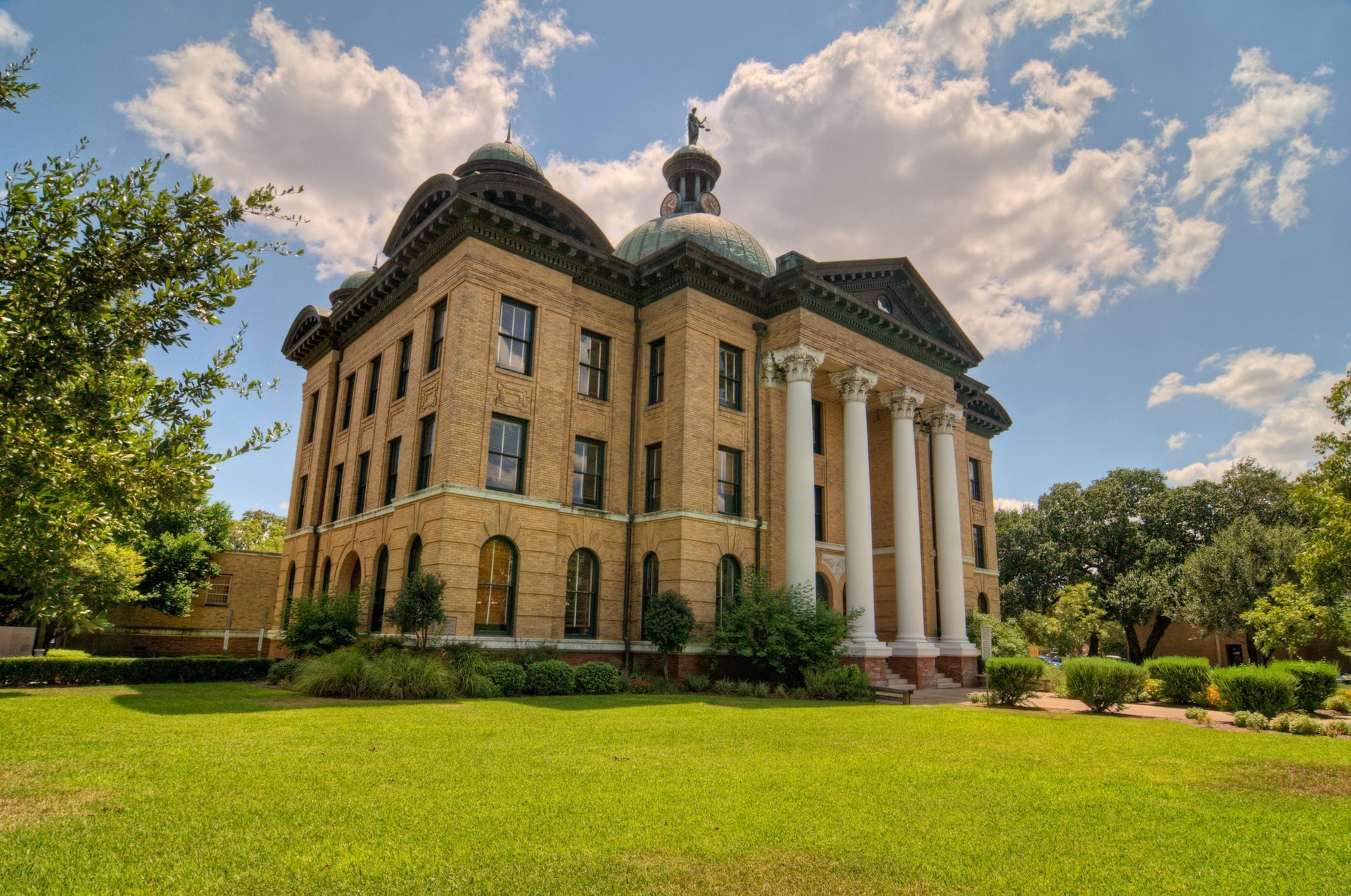 Historic brick building with a dome, white columns, and green lawn under a partly cloudy sky.