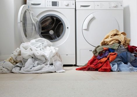 Washing machine with open door and dryer; piles of white and colored laundry on the floor.
