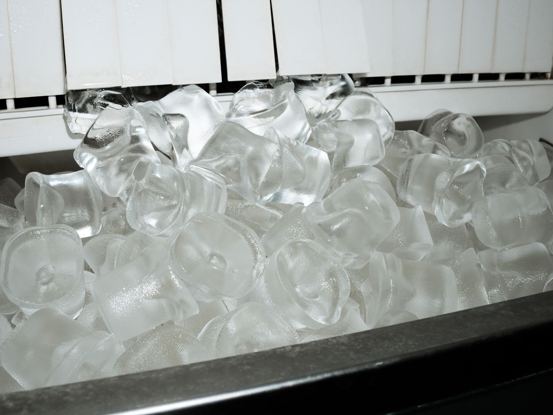 Ice machine dispensing a pile of clear, cylindrical ice cubes into a bin.
