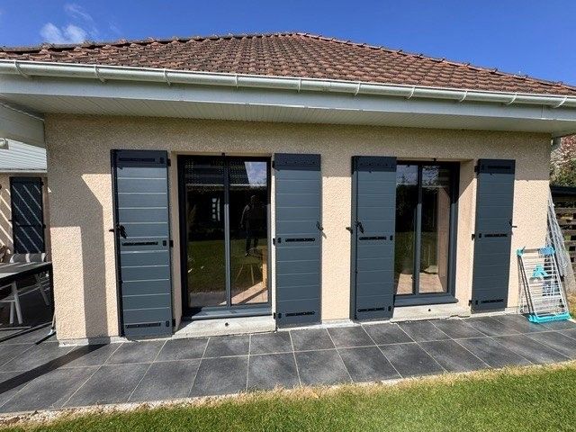 Maison de plain-pied avec volets bleus, portes vitrées et terrasse carrelée