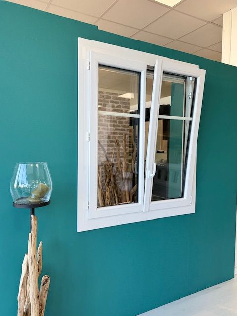 Mur turquoise avec une fenêtre blanche et un bol décoratif en verre sur un support en bois flotté
