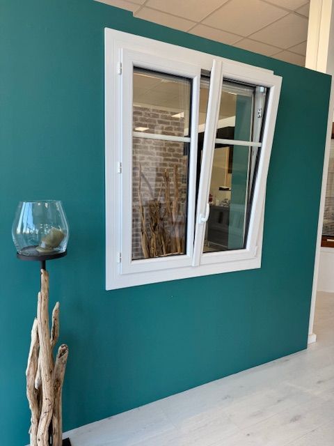 Mur turquoise avec une fenêtre à cadre blanc et un vase décoratif en verre sur un support en bois flotté