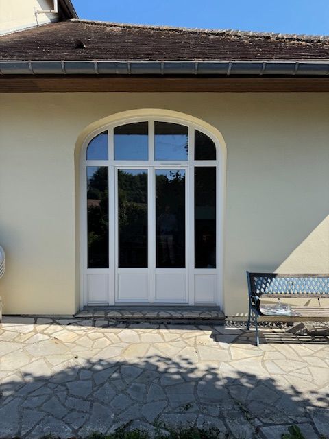 Double porte vitrée cintrée blanche sur une maison en stuc avec terrasse en pierre et banc à proximité