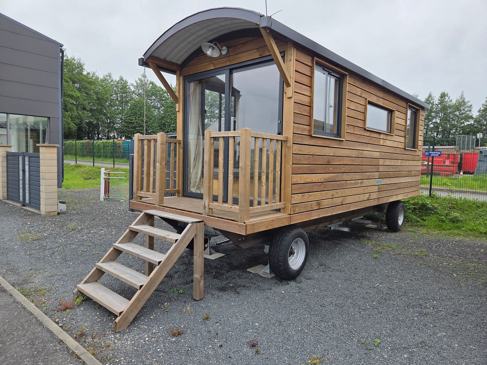 Petite maison en bois sur roues avec marches et porche, garée sur du gravier à l'extérieur