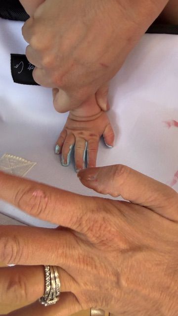 child handprint being pressed onto The Stever Co Mom’s Favorite insulated tote with blue paint