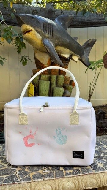 Mom’s Favorite white insulated tote bag by The Stever Co. decorated with children’s handprints and displayed outdoors in front of a shark sculpture.
