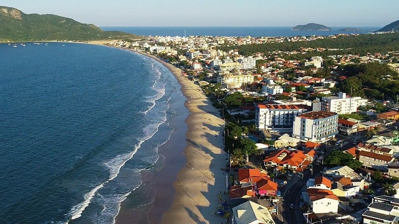 Vista aérea de uma cidade costeira com uma longa praia de areia, água azul e edifícios residenciais que se estendem ao longo da costa.