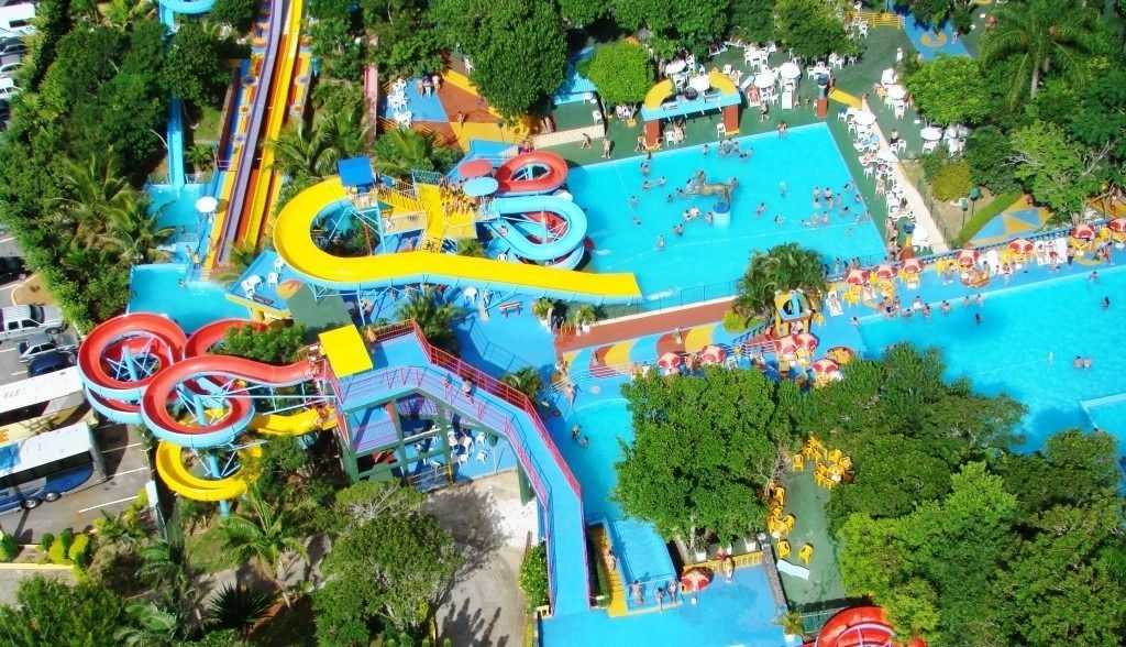Vista aérea de um parque aquático com toboáguas coloridos, piscinas interligadas e uma exuberante vegetação ao redor.
