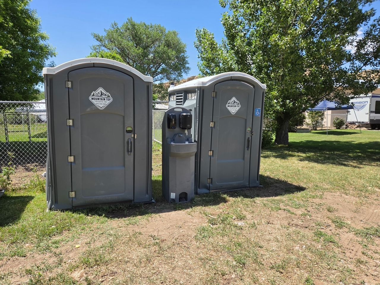 Three blue portable toilets standing on a dirt clearing near trees