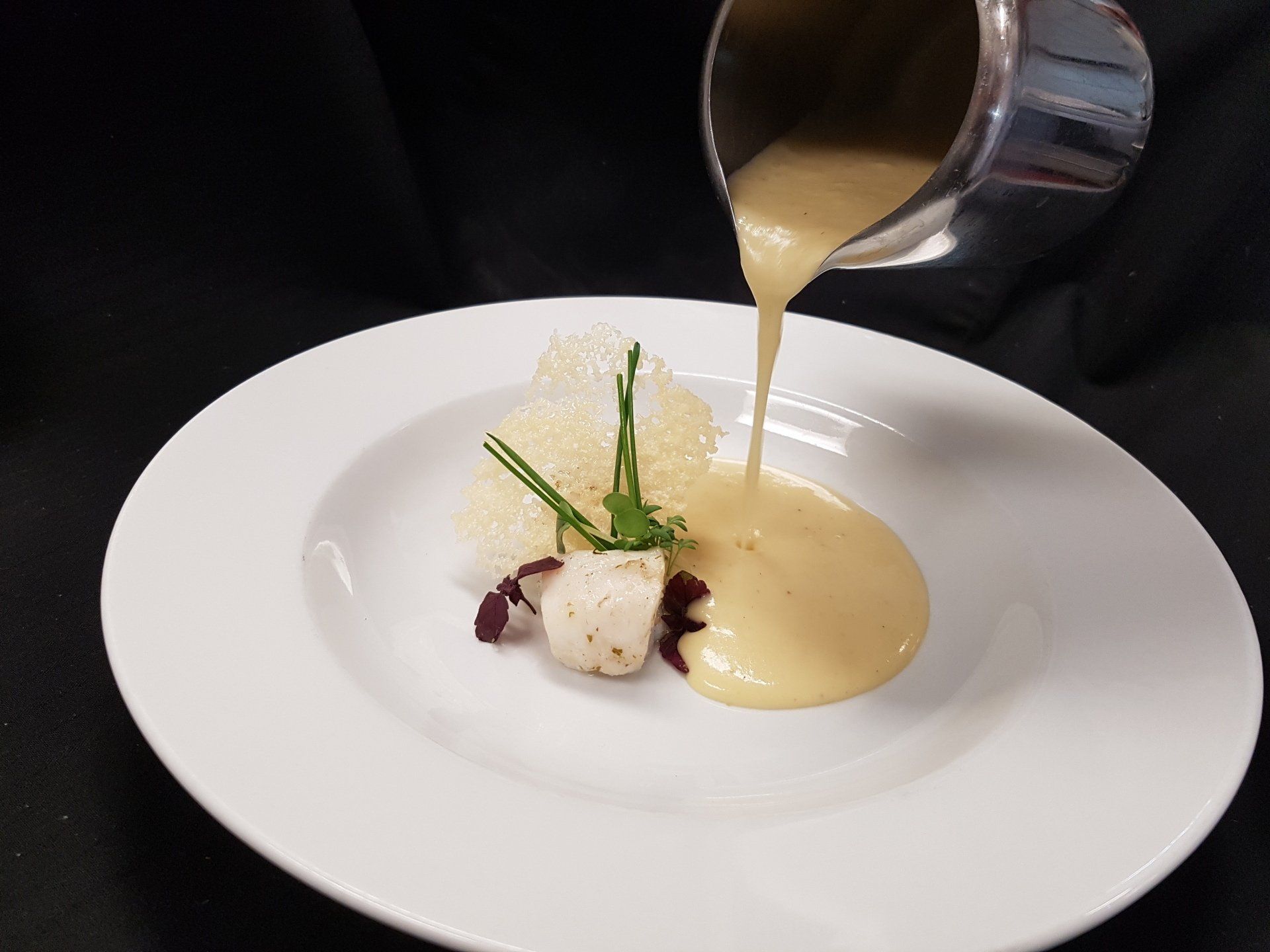 Creamy sauce being poured over a plated appetizer with garnishes.