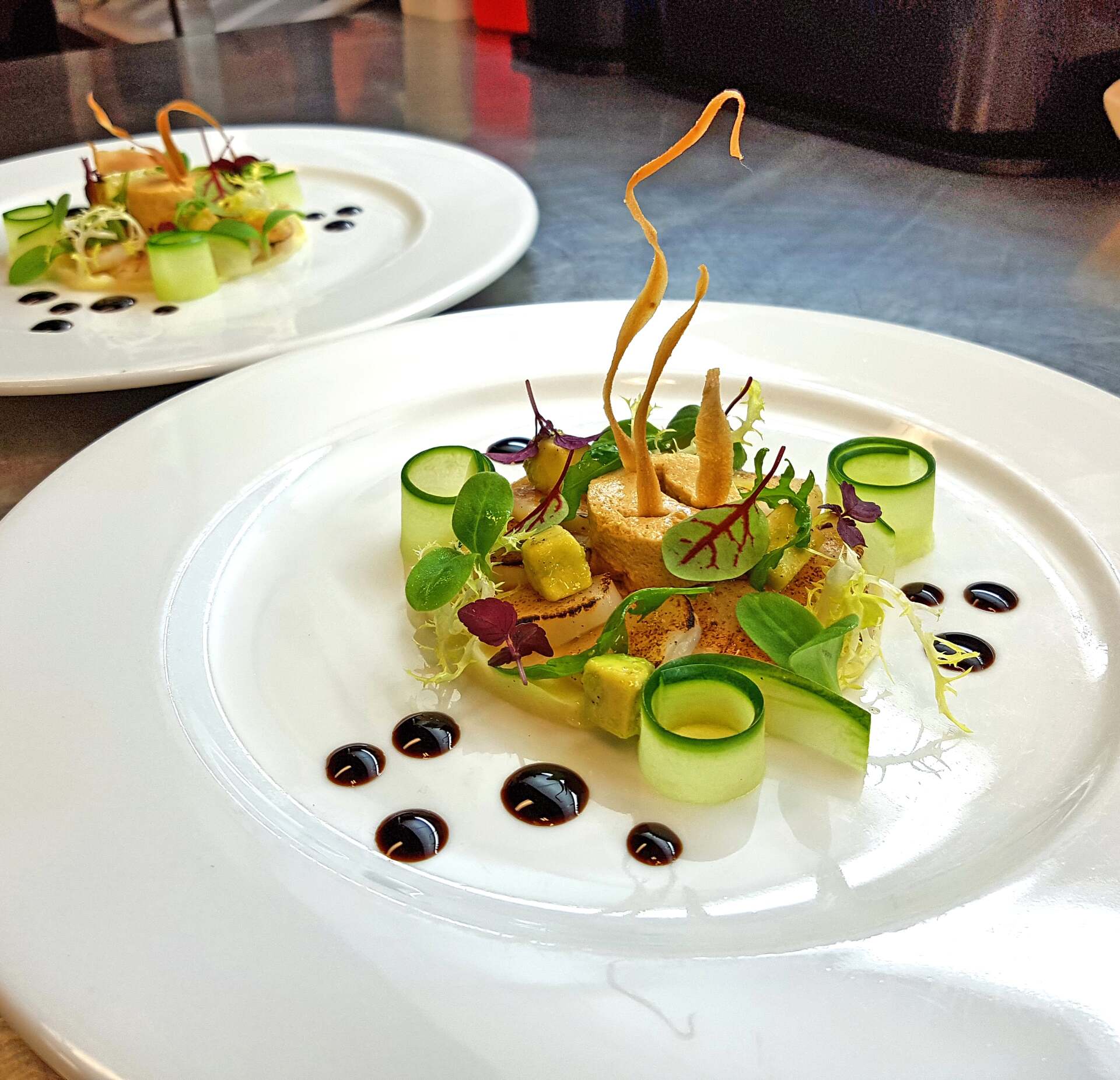 Two plates of gourmet food with cucumbers, avocado, sauce, and fried garnish.