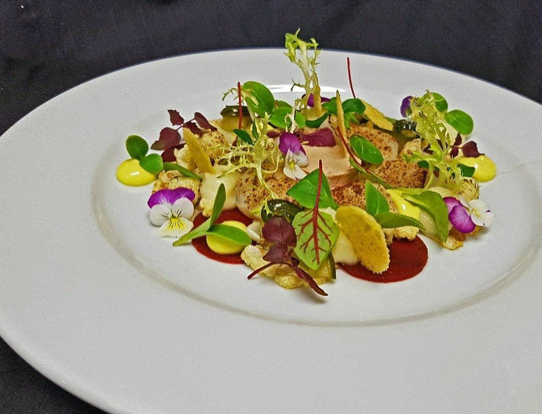 Gourmet plate of food: seared fish with vegetables, microgreens, and edible flowers on a white plate.